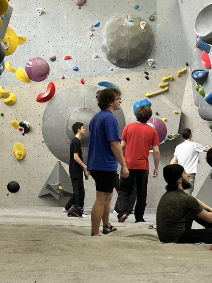 Florian on the mats of a bouldering gym, reading a route on a wall covered in coloured holds