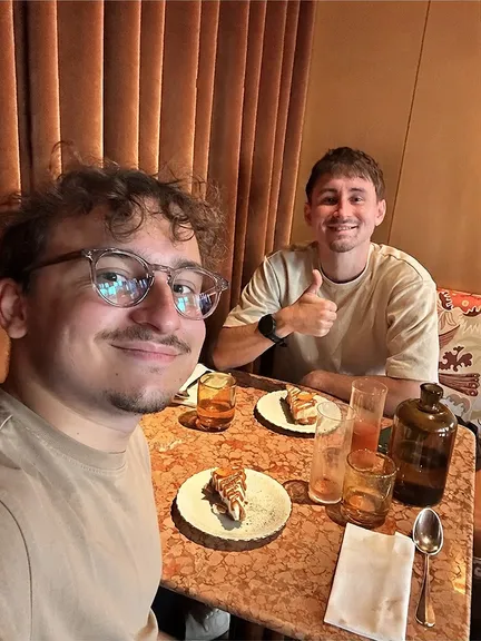 Florian and his brother at a restaurant table, his brother giving a thumbs up behind two slices of caramel cake
