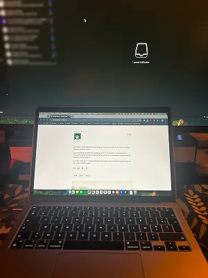 A laptop on a desk at night showing this portfolio's home page, in front of a large monitor
